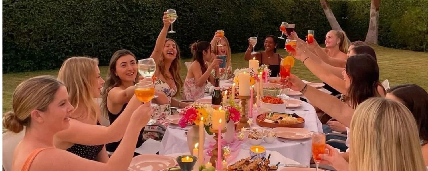 A group of women laughing and toasting around a dinner table